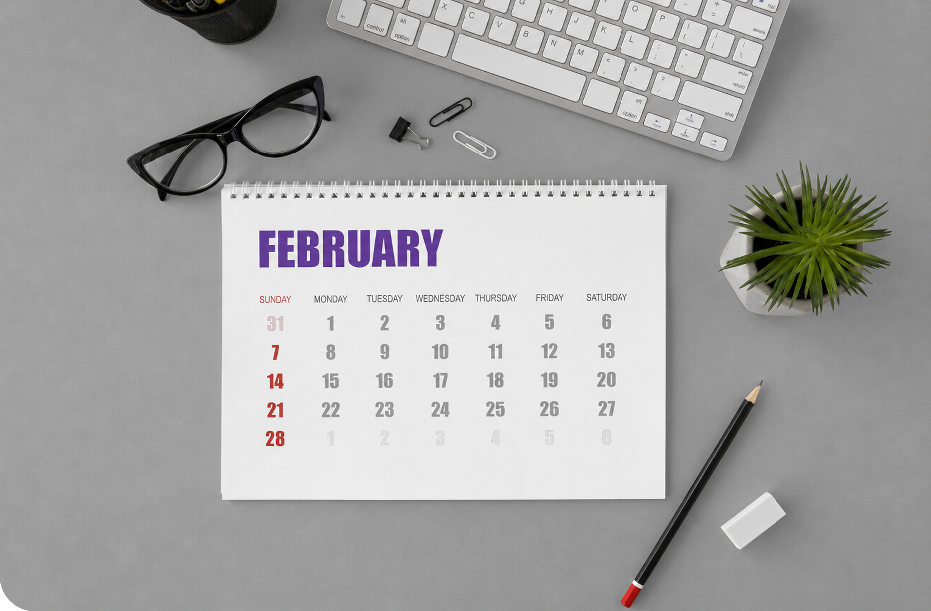 A desk calendar beside a keyboard and glasses